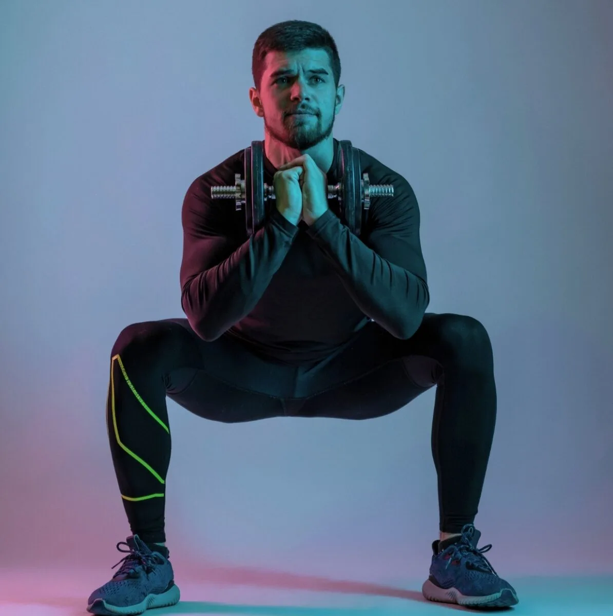 Un homme en tenue de sport effectuant un squat sumo avec des haltères.